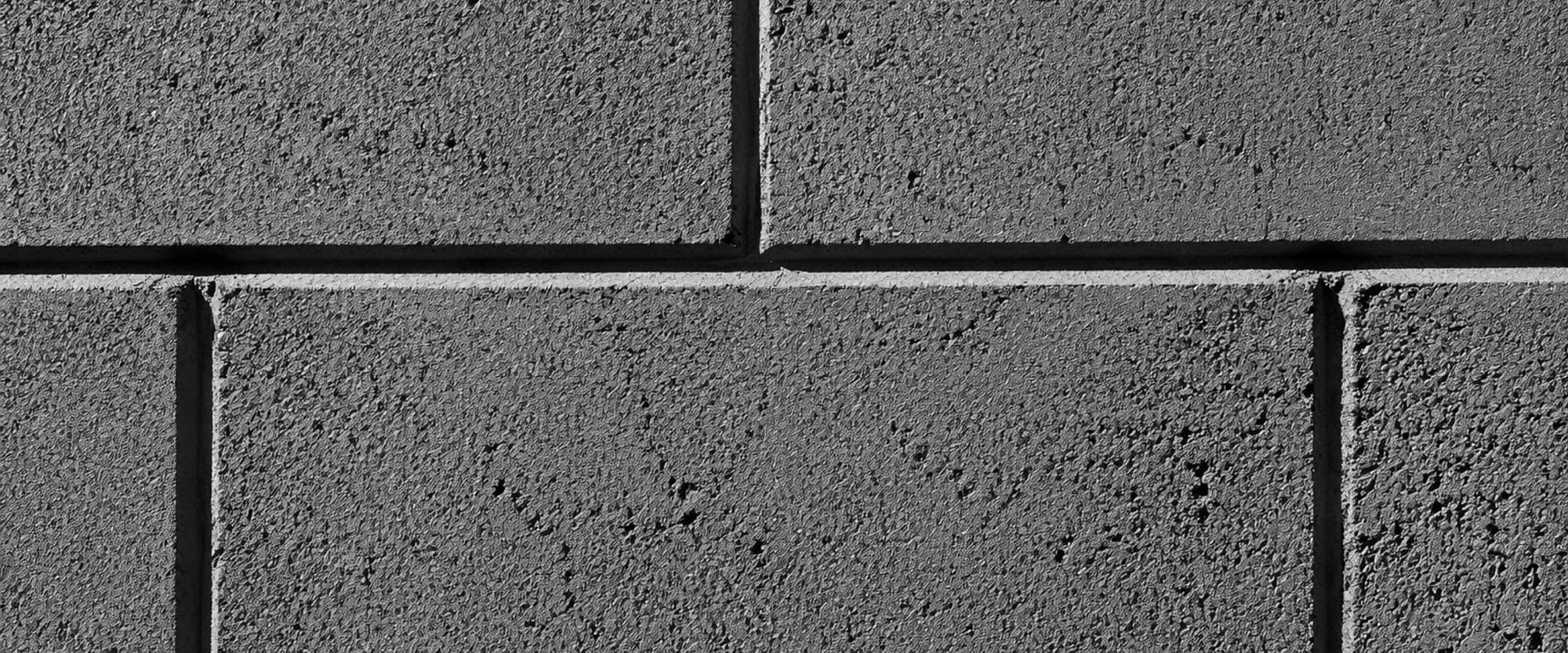 Raking light across a precisely laid concrete block wall, every mortar joint reading as a sharp shadow line